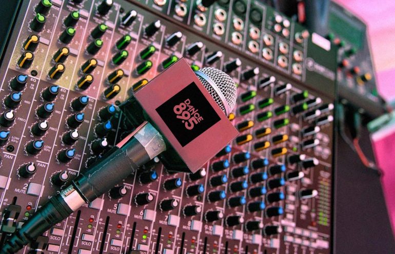 A microphone labeled "Dance 89.5" resting on a sound mixing console with various colorful knobs and switches.