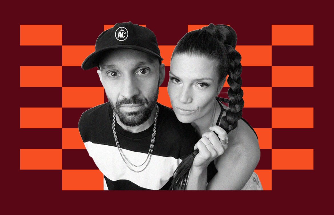 A black and white photo of two people in front of an orange and maroon checkered background. The person on the left wears a cap with an "A" logo. The person on the right has a long braided hairstyle.